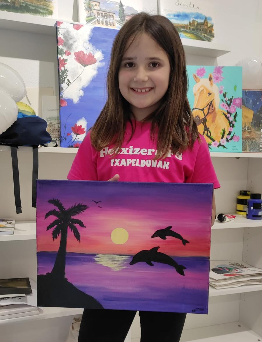 niña sujetando un cuadro pintado por ella misma de un paisaje con delfines